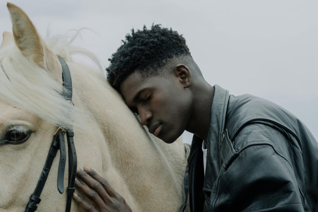 A young man rests his head affectionately on a white horse outdoors.